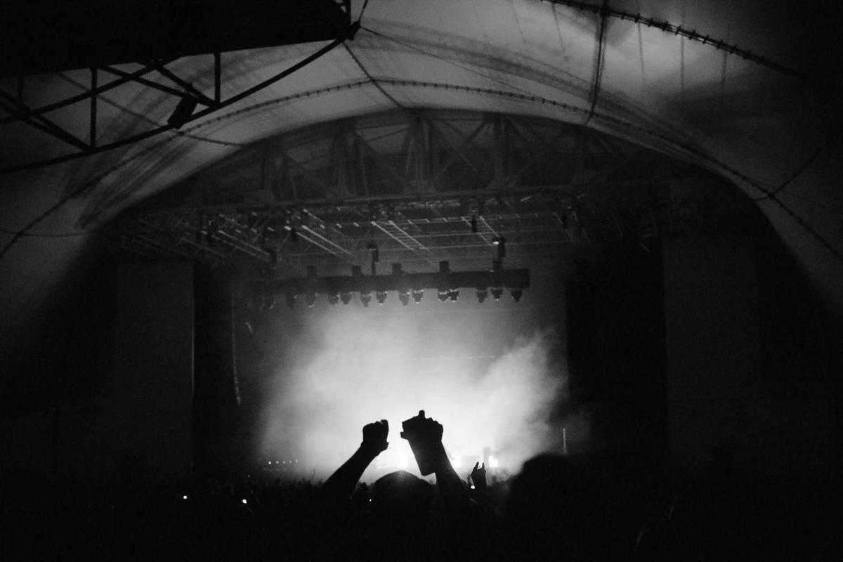 Concert crowd with raised hands silhouetted against a smoky stage