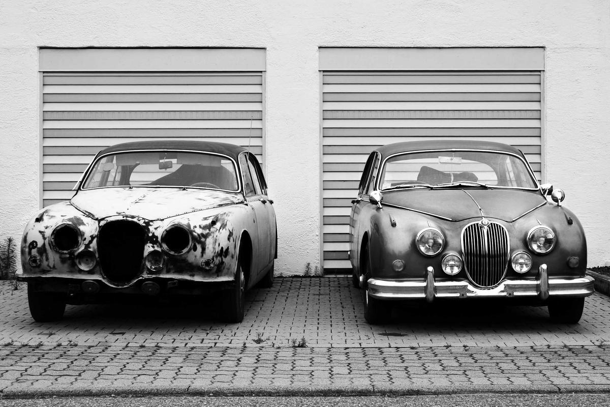 Two classic cars parked in front of garage doors